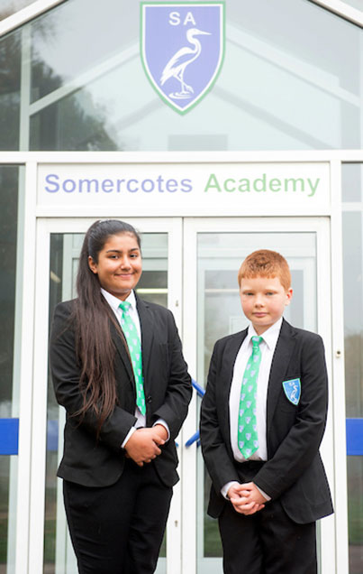 A boy and a girl student stood wearing the academy lower school uniform